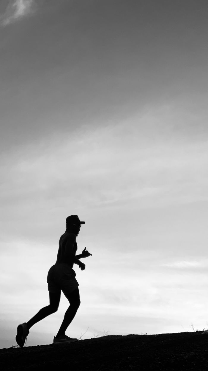 A silhouette of a man running uphill during twilight, emphasizing movement and fitness.