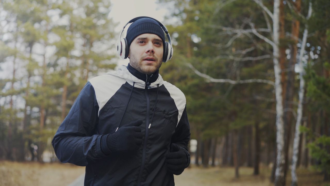 Young man jogging outdoors in winter wearing headphones and jacket for warmth.