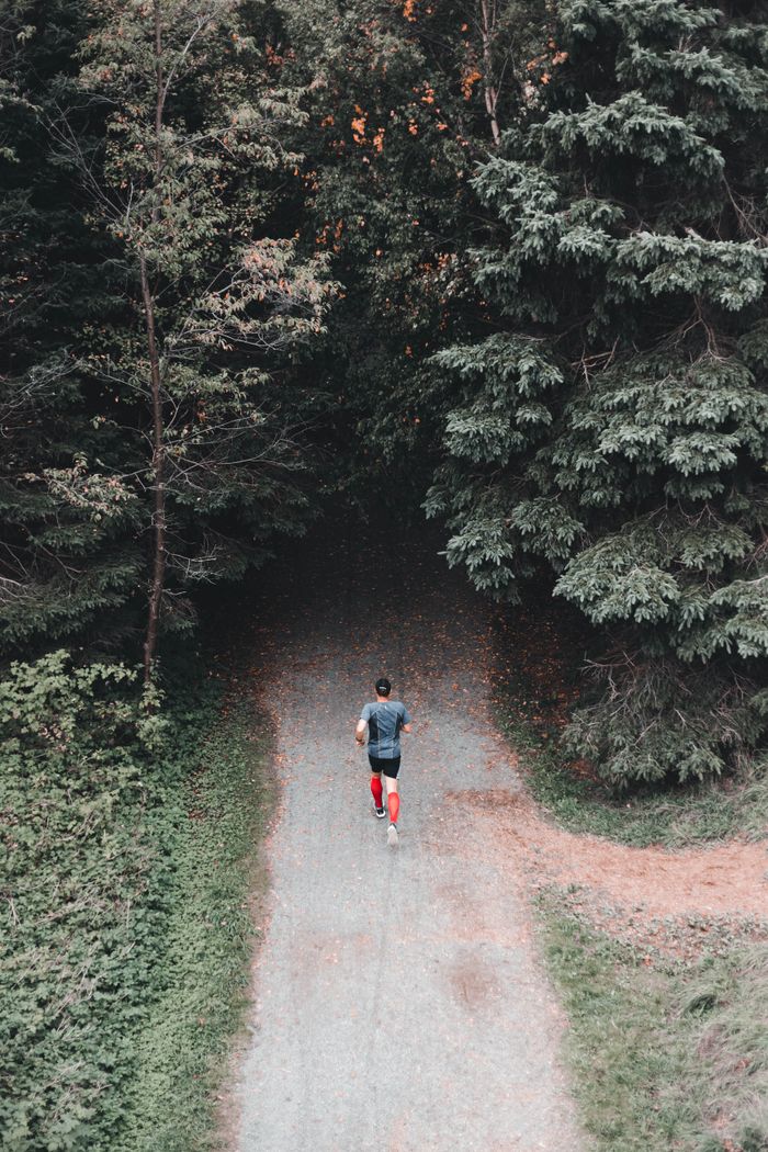 Aerial view of a man jogging on a winding forest trail during the day.